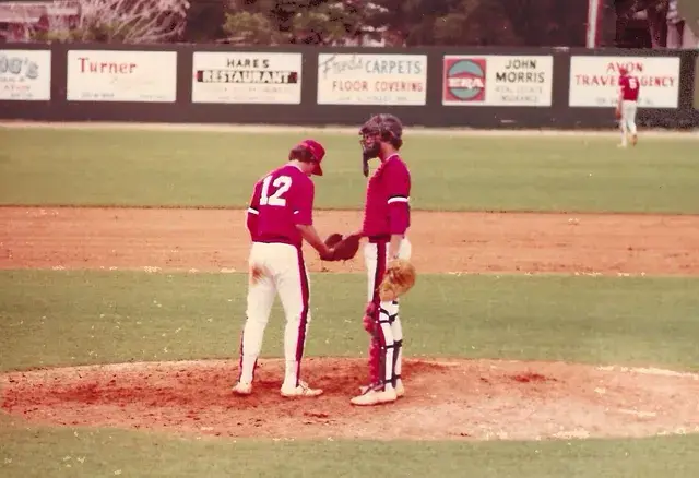 Pitcher number 12 and the catcher confer on the mound in red uniforms.