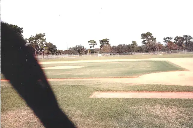 The infield of an empty diamond seen from the first-base side, a shadow across the print.