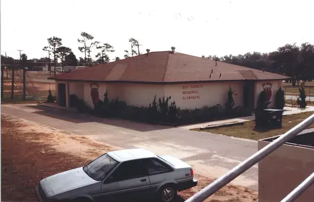 The Guy Barrett Memorial Clubhouse, a low block building with painted emblems, a car parked in front.