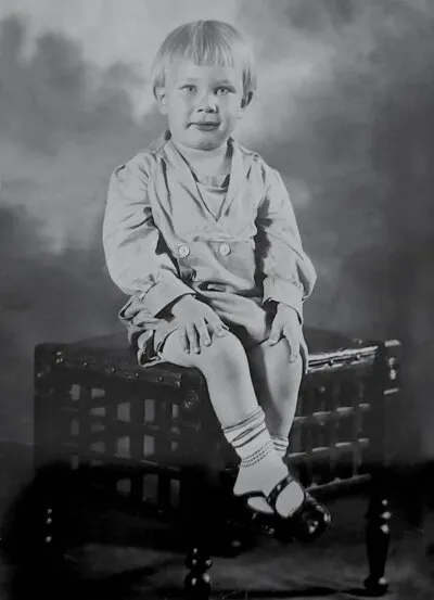 Pharis Weekley as a small boy, seated on a wicker bench in a studio portrait.