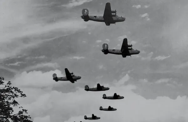 Six B-24 Liberator bombers in formation above the clouds.