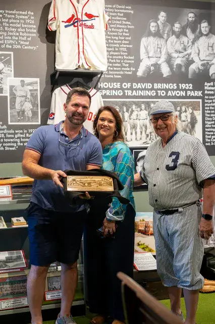 Three people pose with a plaque beside the House of David spring training panel.