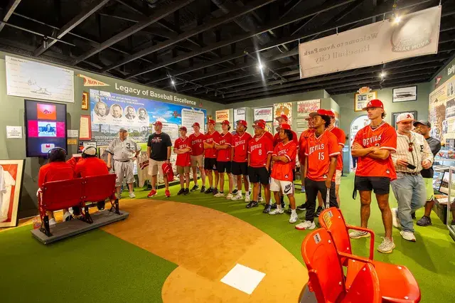 The Devils team lines the infield turf beneath the Legacy of Baseball Excellence panels.