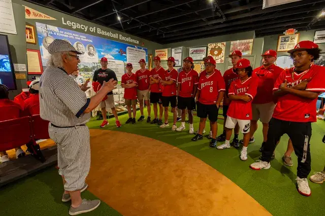 The man in the vintage pinstriped number 3 uniform talks to the team gathered around the turf.