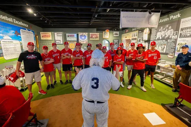 The man in the vintage pinstriped number 3 uniform, seen from behind, faces the team in red.