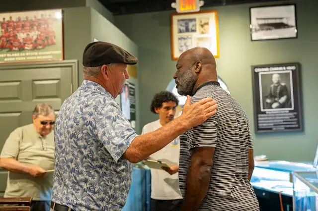Two men greet each other, one with a hand on the other's shoulder.