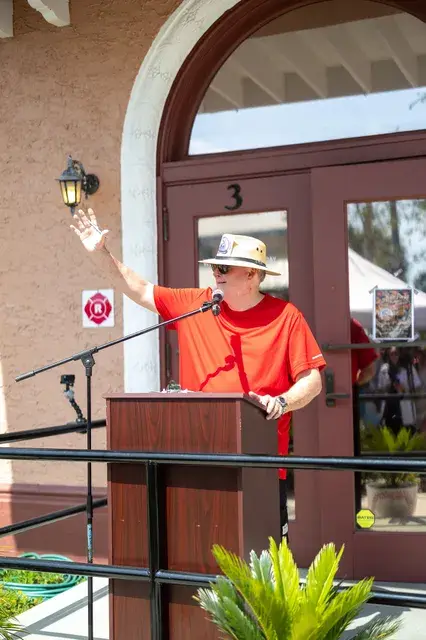 A man in a red shirt waves from the podium.