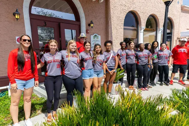The softball team in grey jerseys pose along the porch.