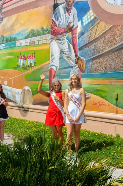 Two pageant winners in front of the mural's pitcher.