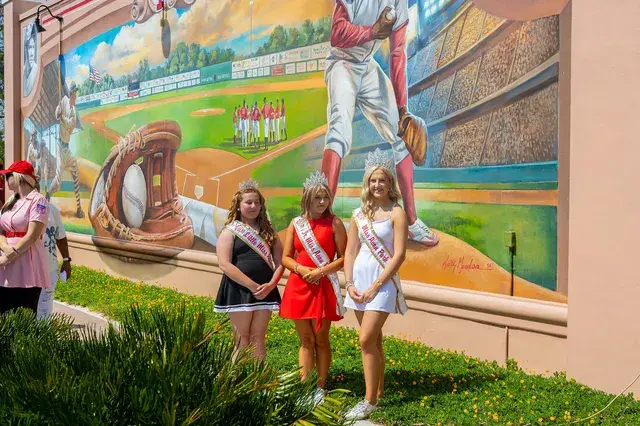 Three pageant winners in front of the mural.
