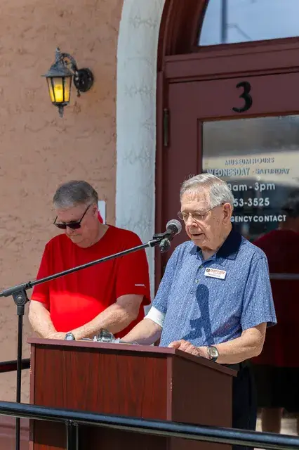 Two men at the podium, one reading from a page.