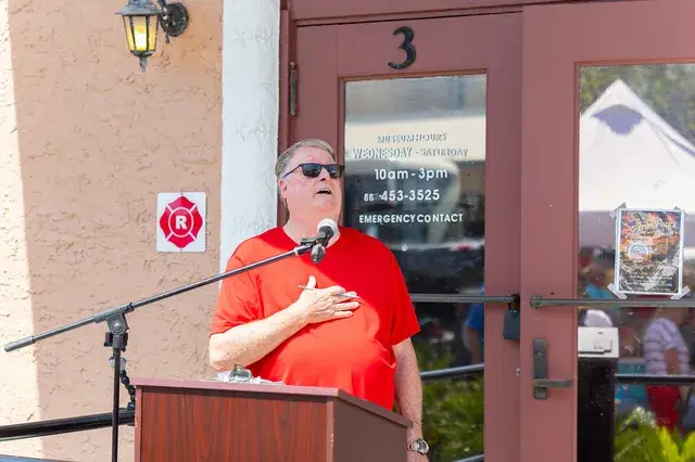 A man in red with a hand on his heart at the podium.