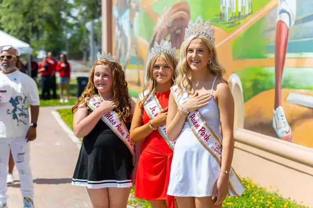 Three pageant winners with hands on hearts in front of the mural.