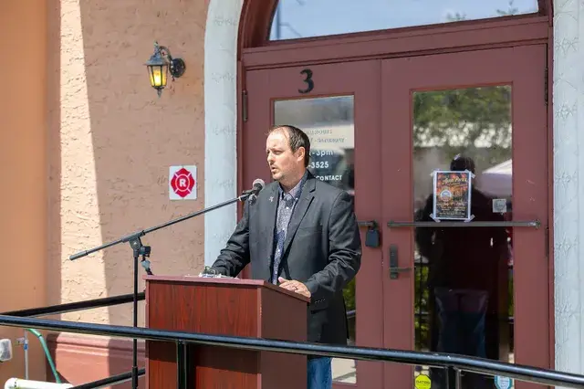 A man in a grey jacket speaks at the podium.