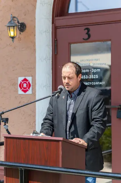 The man in the grey jacket at the podium, looking down at his notes.
