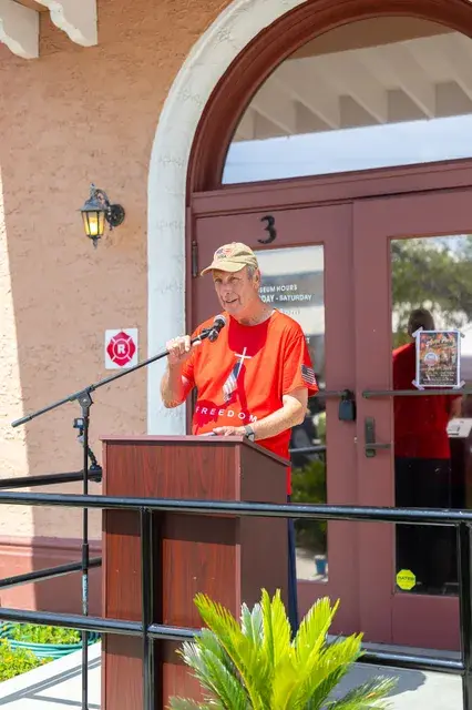 A man in a red Freedom shirt speaks at the podium.