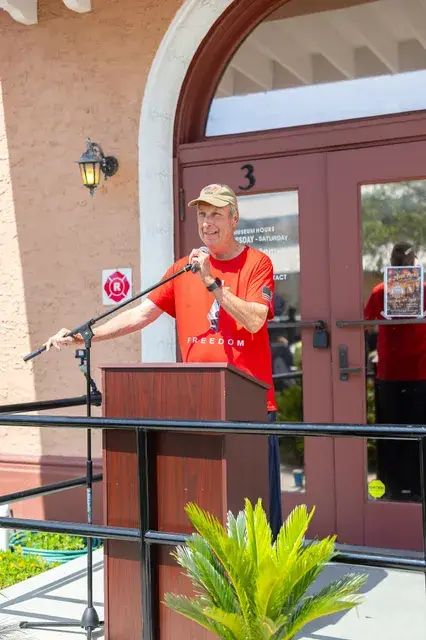 The man in the red shirt gestures at the podium.