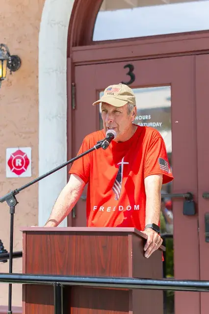 The man in the red shirt speaks with both hands on the podium.