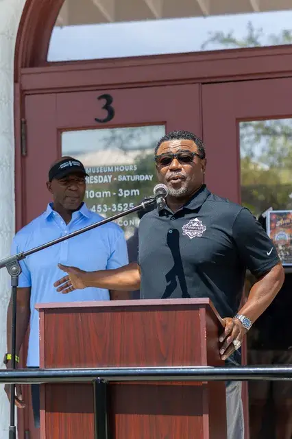 The man in the black polo gestures as he speaks.