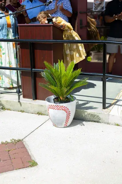 A woman in gold at the podium, a planter painted like a baseball below.