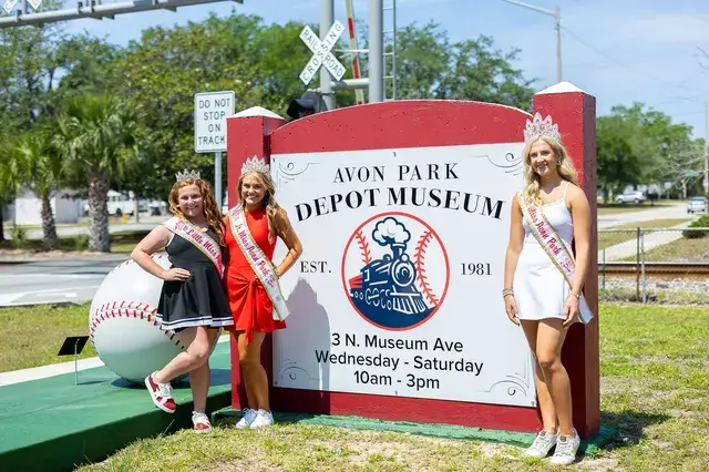 Three pageant winners at the Depot Museum sign.
