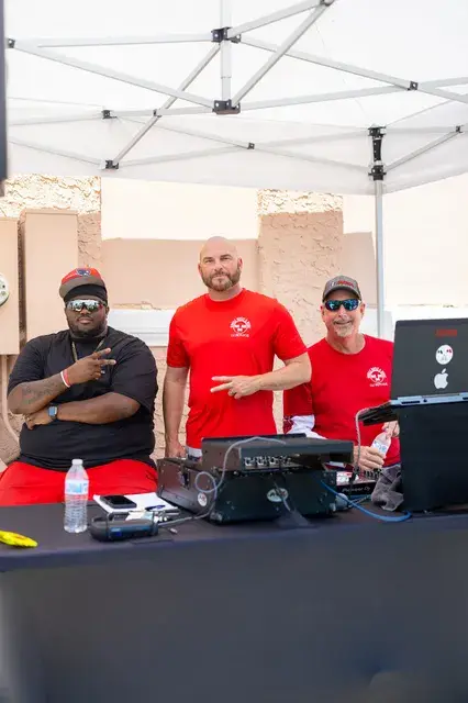 Three men at a DJ table under a tent.