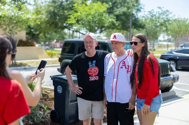 Three people pose by a Jeep, one in a white AP jersey.