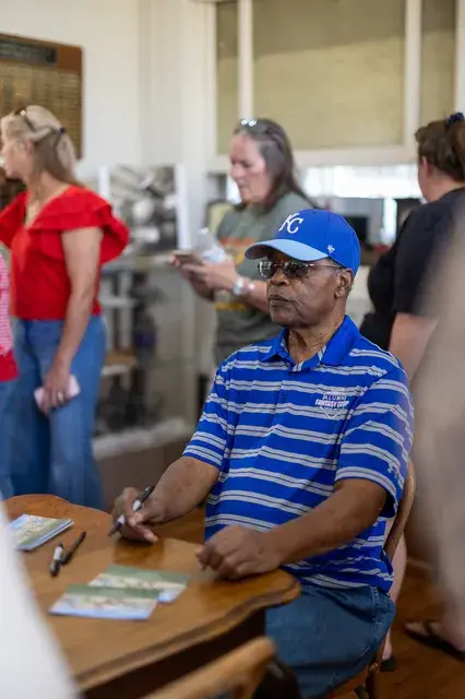 A man in a striped shirt signs cards at a table.