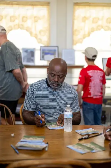 The man in the striped shirt signing, seen from the side.