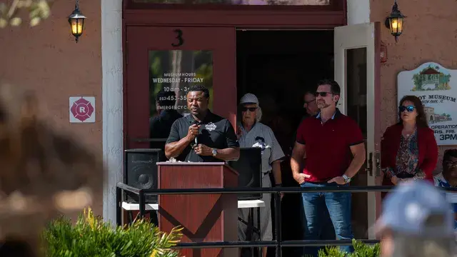 The speaker at the podium with a man in a red polo and a woman in red listening beside him.