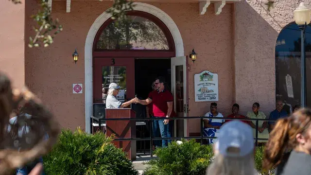The Depot entrance with a speaker gesturing from the podium and guests seated along the porch.