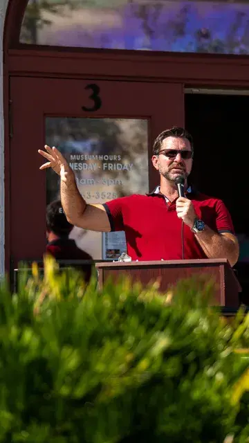 The speaker in the red polo raises a hand as he talks at the podium.