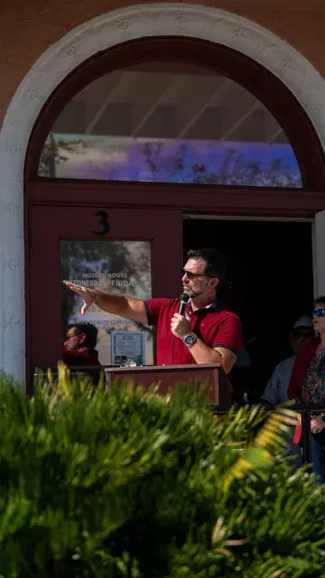 The speaker in the red polo points across the crowd, framed by the Depot's arch.