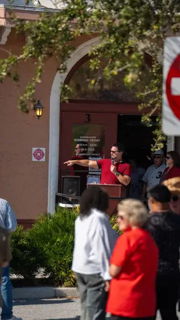 Guests on the lawn, a woman in red in the foreground, as the speaker points.