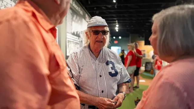 Inside the museum, the man in the vintage pinstriped number 3 uniform talks with guests among the exhibit panels.