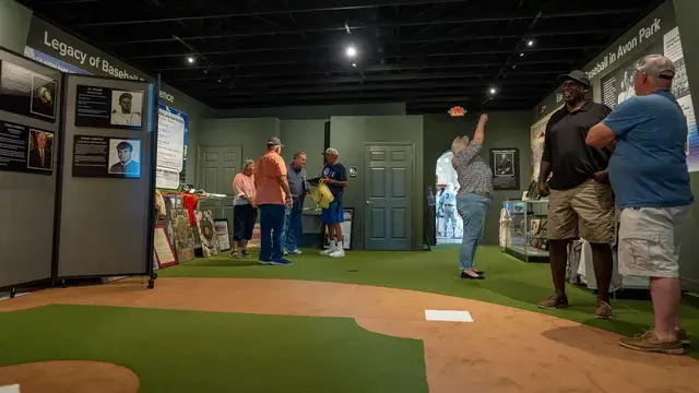 The museum's main gallery: a green turf floor marked as an infield, exhibit panels and visitors.
