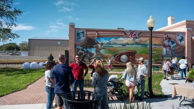 Guests mingle on the lawn before the mural in bright sun.