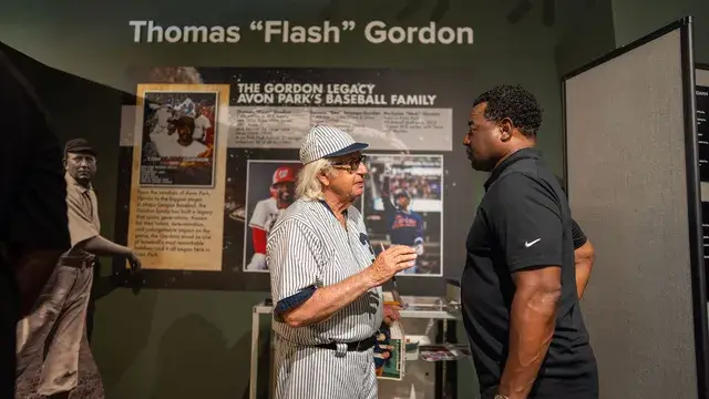 The man in the vintage pinstriped number 3 uniform talks with a man in black beside the Thomas Flash Gordon panel.
