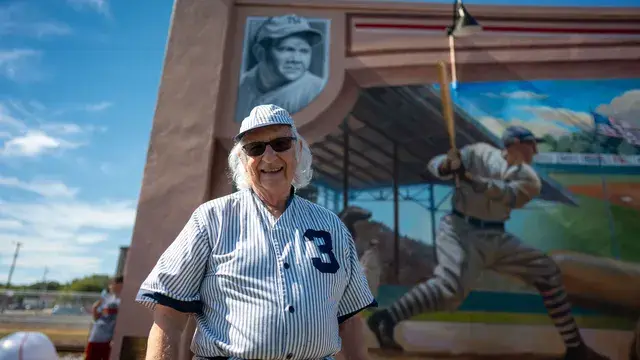 The man in the vintage pinstriped number 3 uniform smiles in front of the mural's batter.