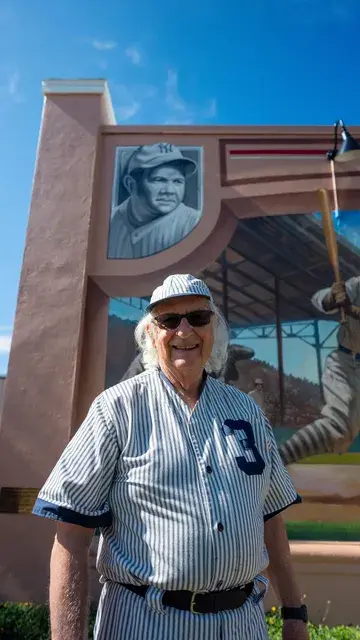The man in the vintage pinstriped number 3 uniform in front of the mural, portrait format.