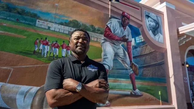 The man in the black polo smiles beneath the mural's pitcher.