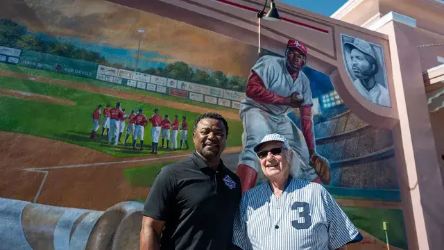 The same two men laugh together in front of the mural.
