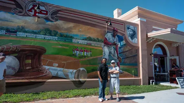 A couple stand at the base of the mural beneath the pitcher.