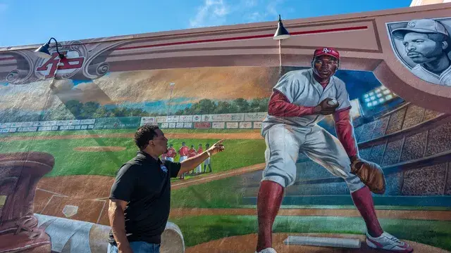 A man in black points up at the mural's pitcher.