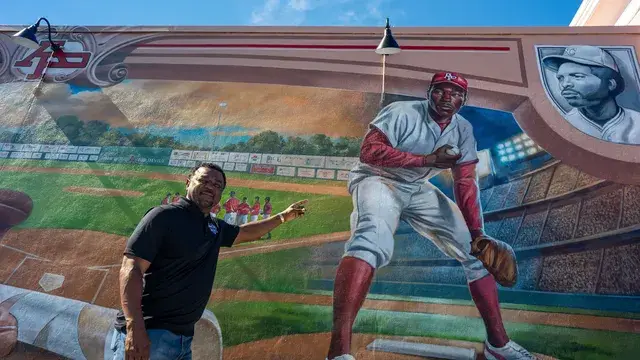 The man in black gestures at the mural's outfield scene.