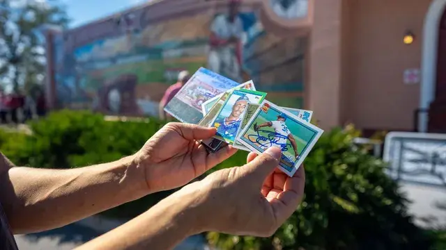 Hands hold up a fan of baseball cards in front of the mural.