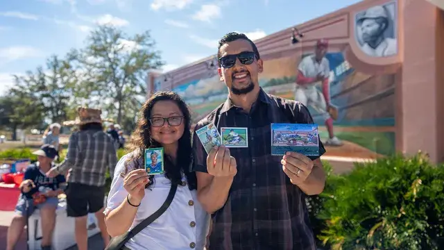 A couple hold up baseball cards in front of the mural.