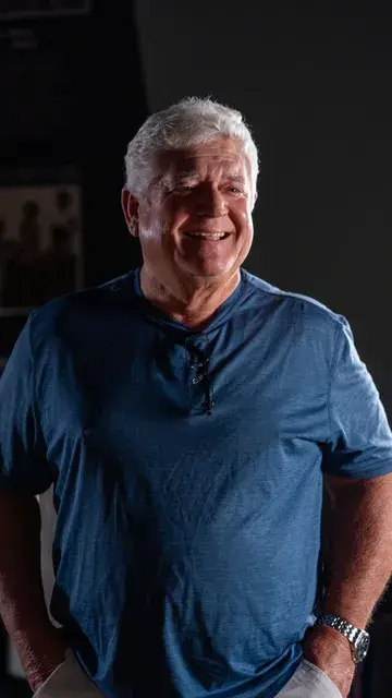 An older man in a blue shirt smiles in the red-lit gallery.