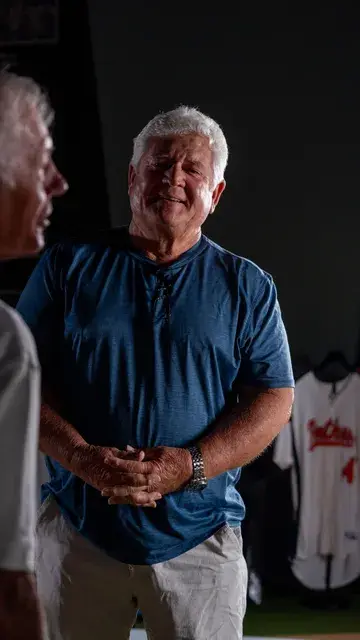 The man in the blue shirt listens beside a display of jerseys.