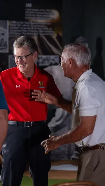 A man in a red polo and glasses laughs with a man in a white polo.
